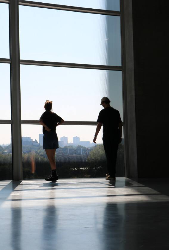 Two people seen from behind at a tall window, looking out over the city